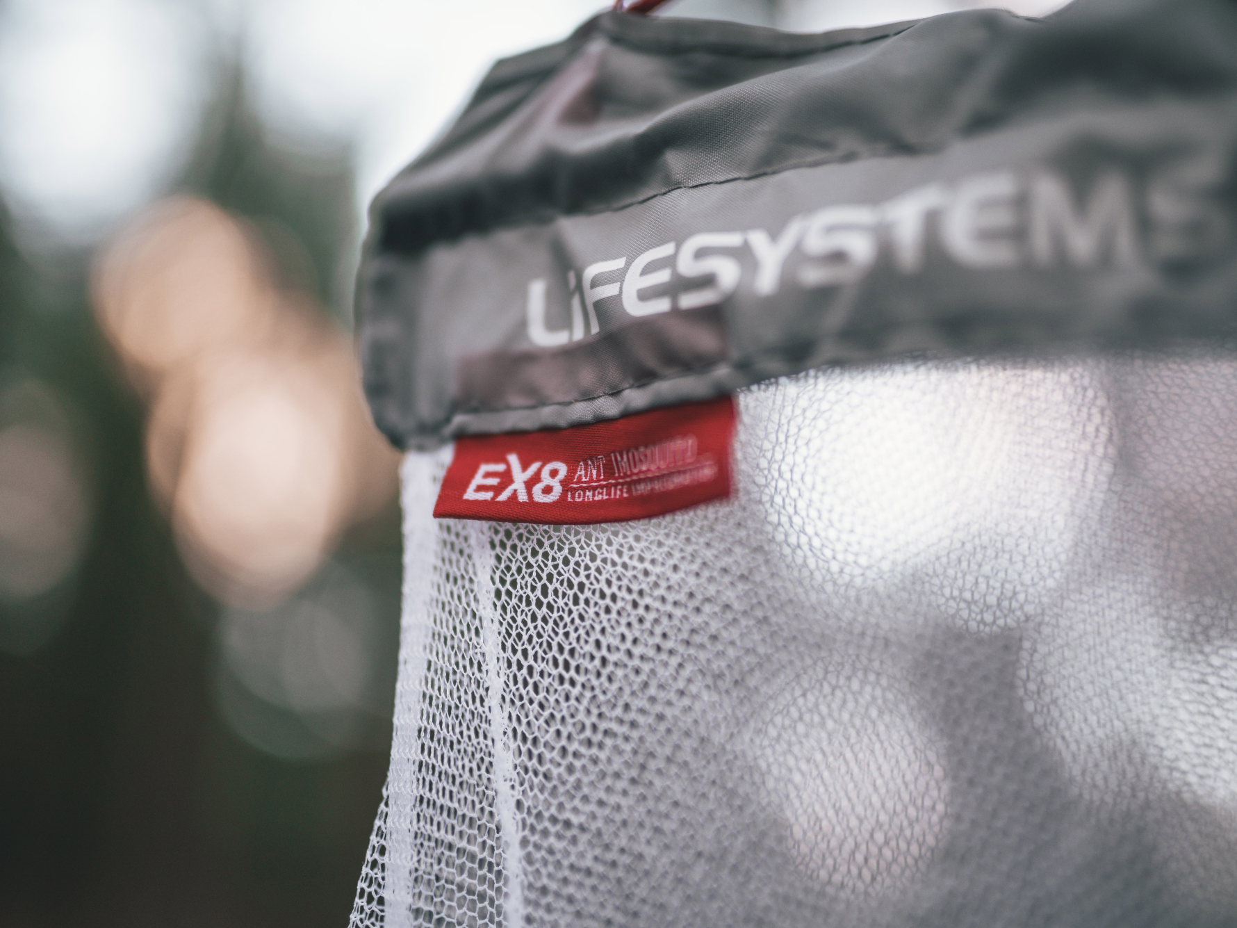 Close-up of a Lifesystems mosquito net with EX8 anti-mosquito treatment label, showing fine mesh detail outdoors.