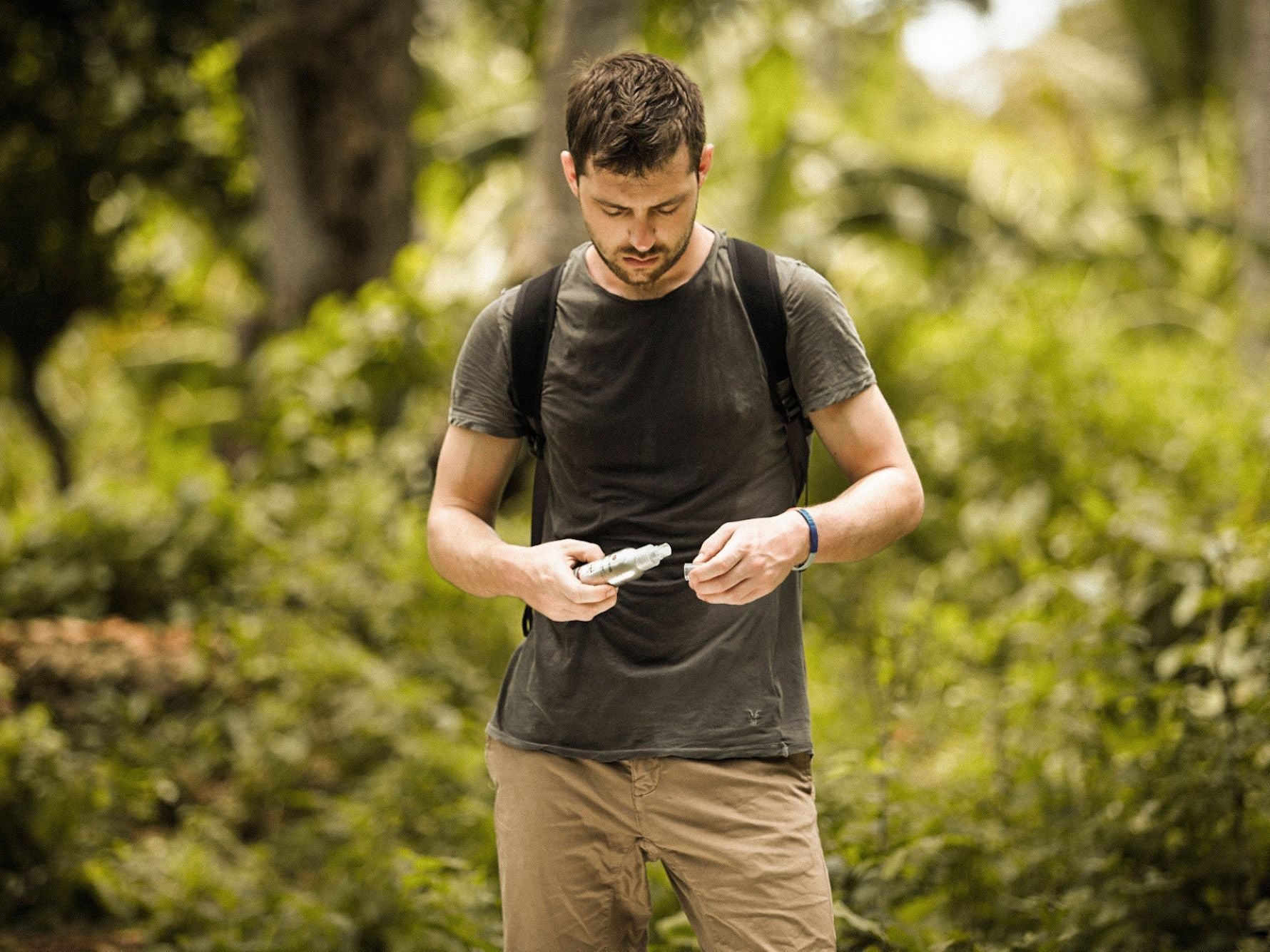 Man applying insect repellent in a tropical forest, wearing a backpack and casual hiking clothes.